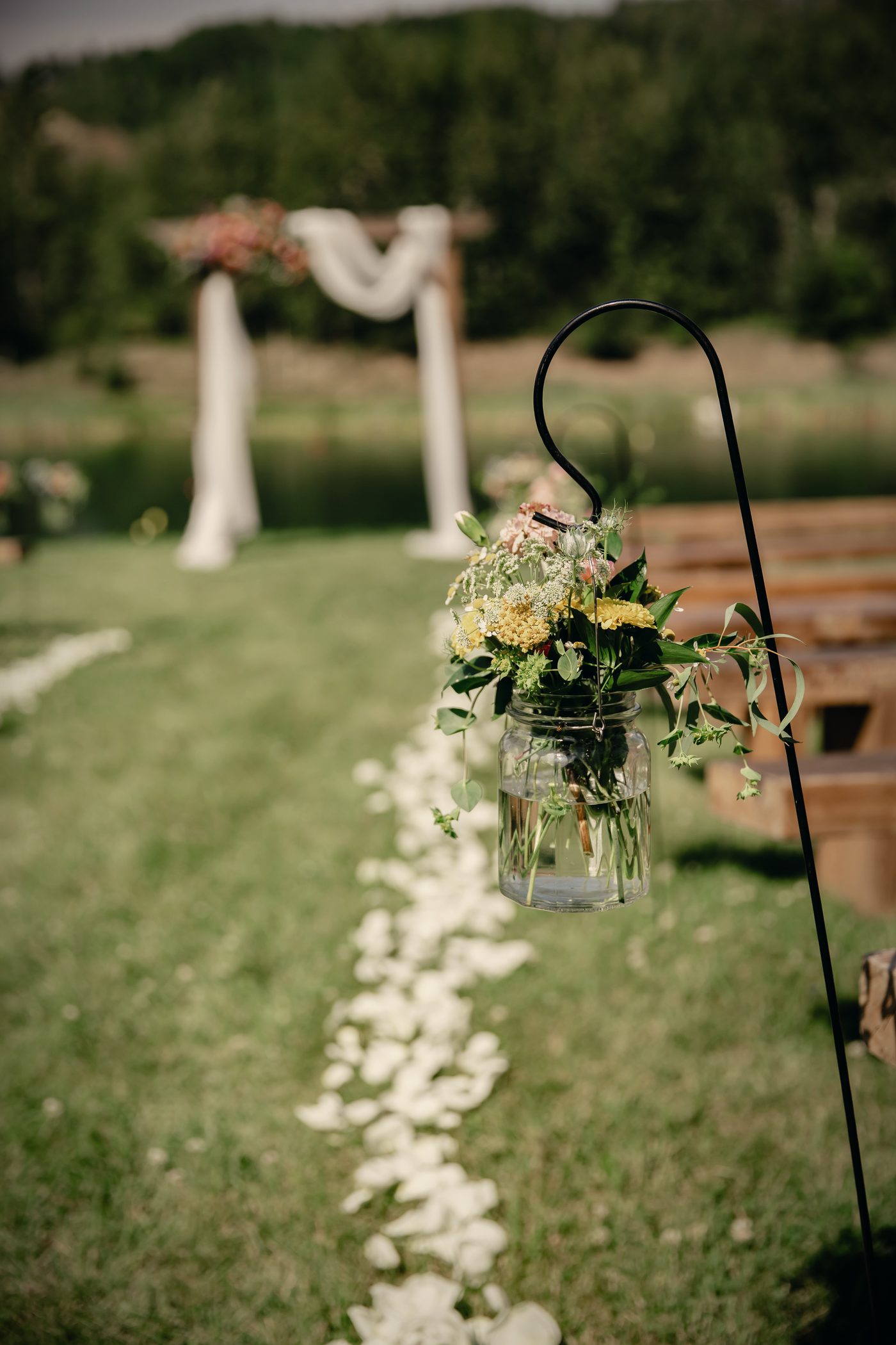 A lantern and white rose petals on the grass beside the aisle, the arbour behind