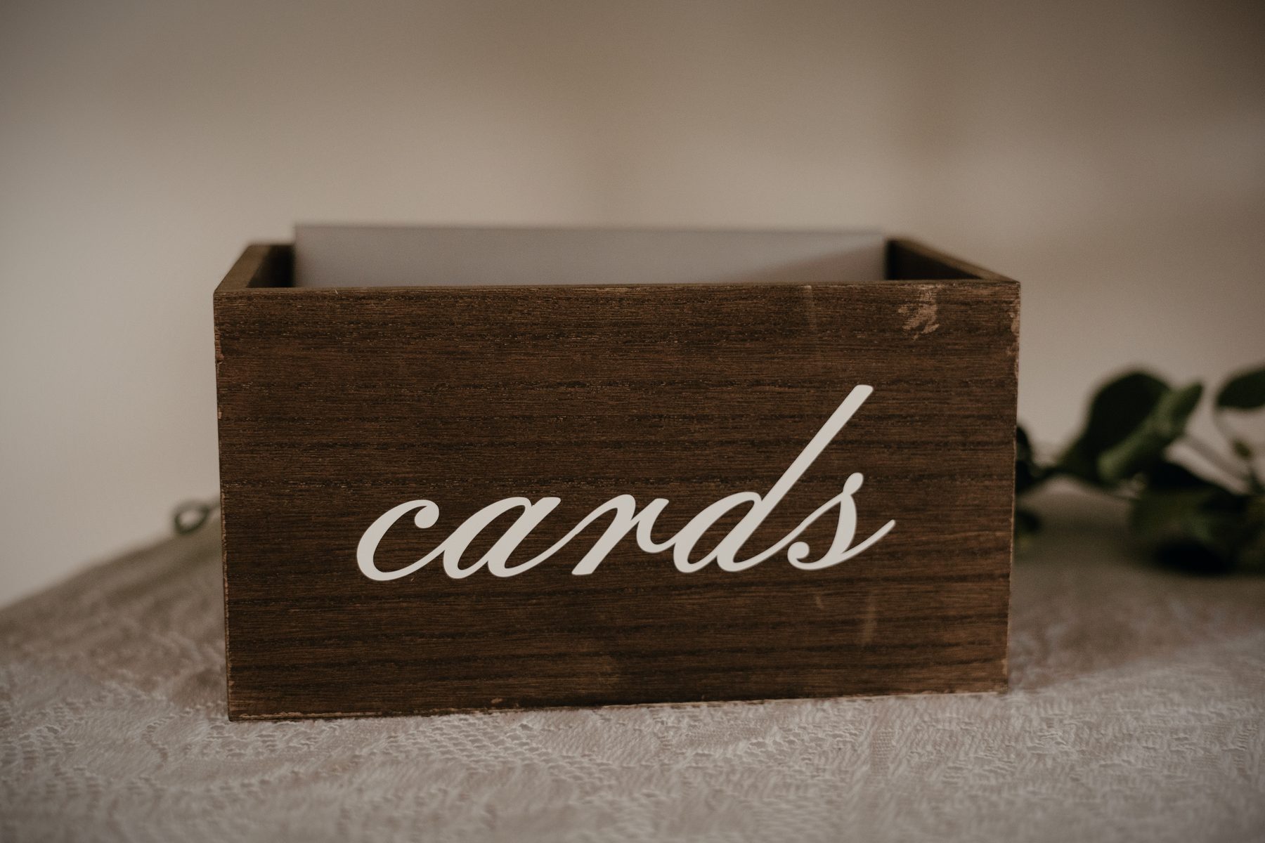 A wooden box lettered 'cards' on lace, trailing greenery beside it