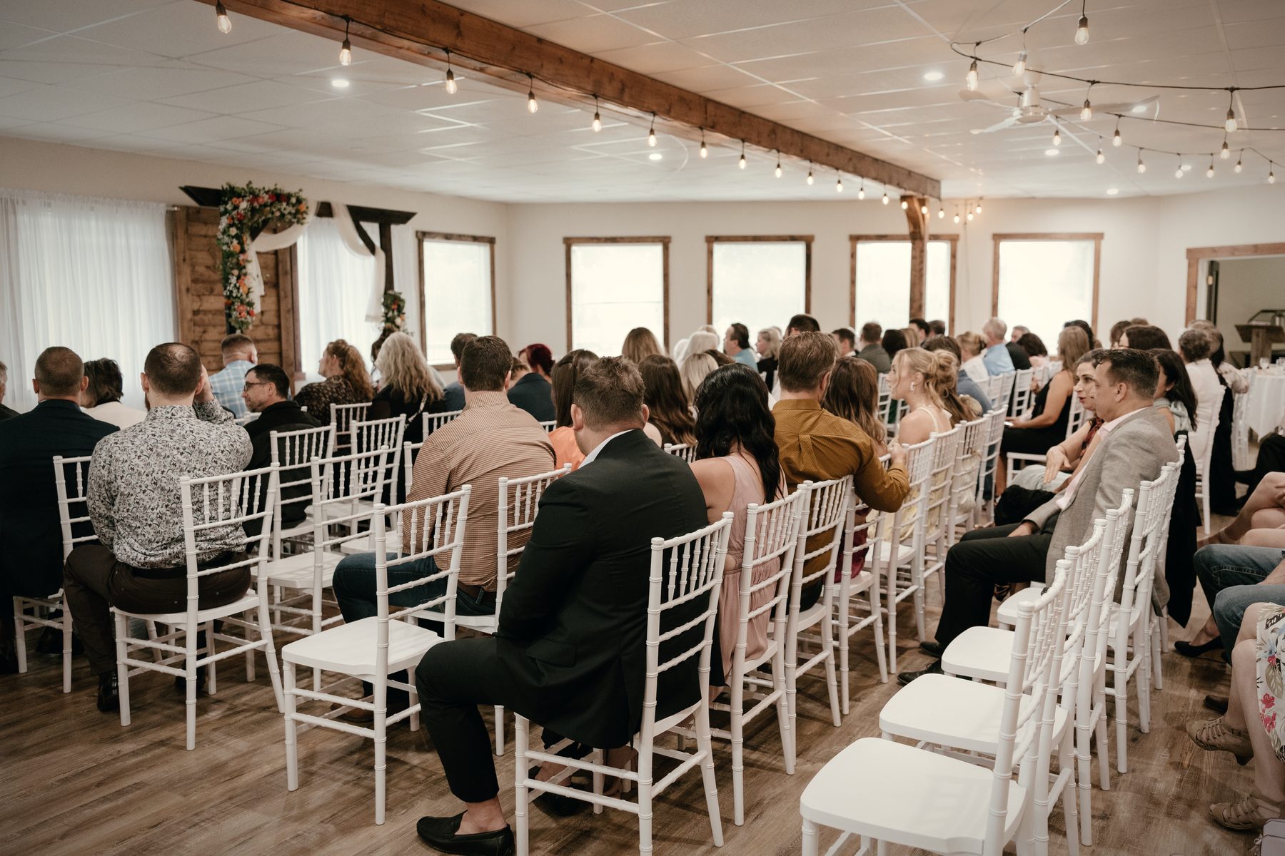 A ceremony in the hall, guests in white chairs down both sides of the aisle, the arch at the far end