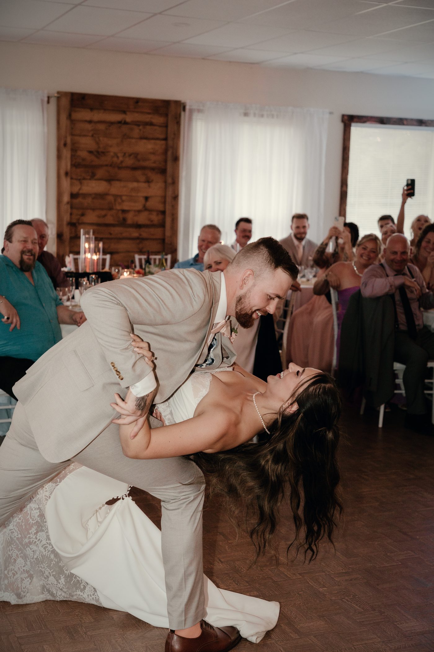 The groom dipping the bride in the hall, wood wall and guests behind them