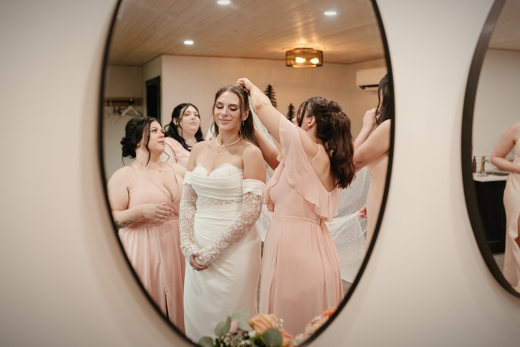 The bride in an oval mirror in the bridal suite, a bridesmaid adjusting her veil