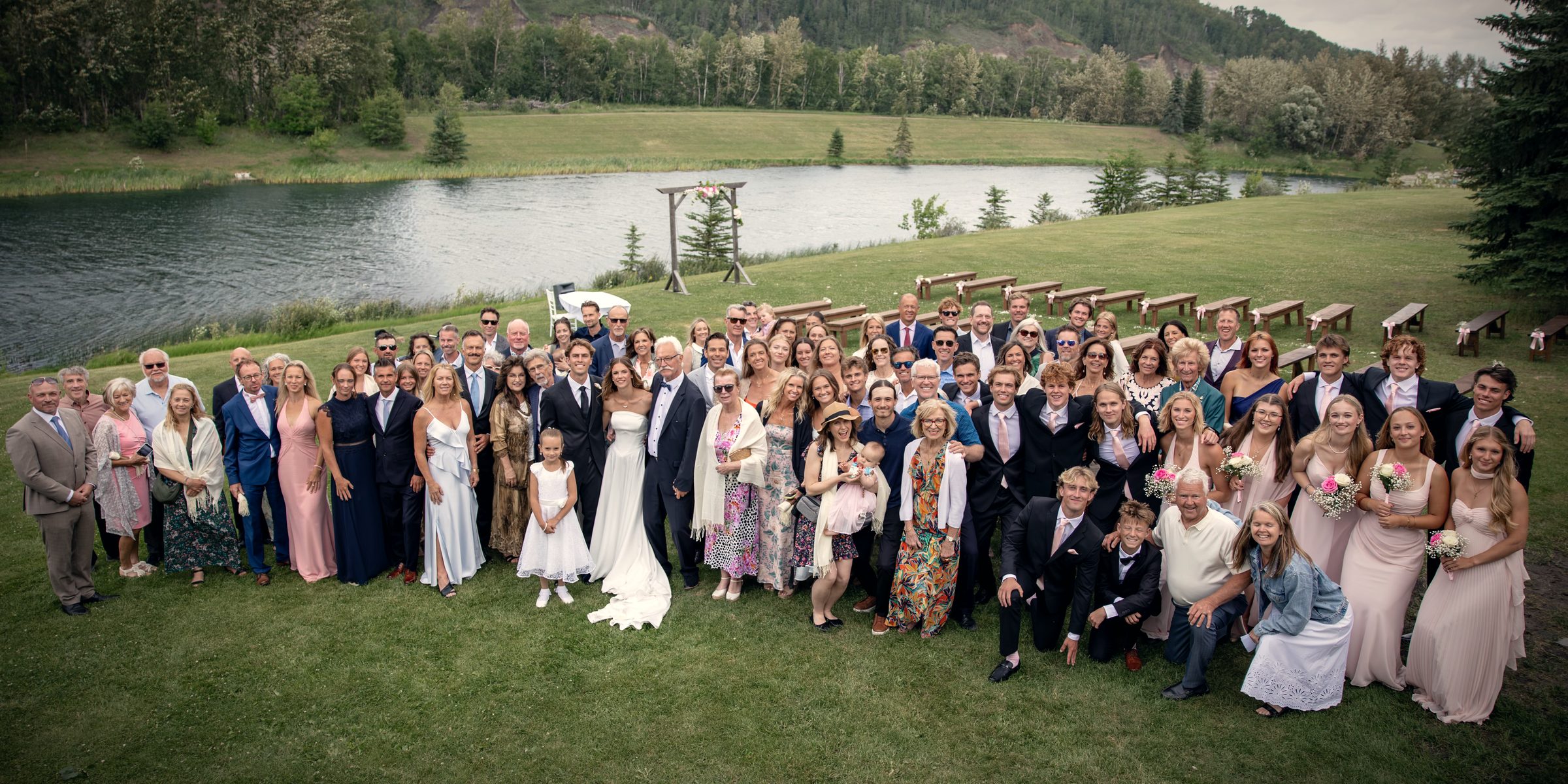 Every guest of a summer wedding gathered on the lawn above the lake, the arbour and the far shore behind them