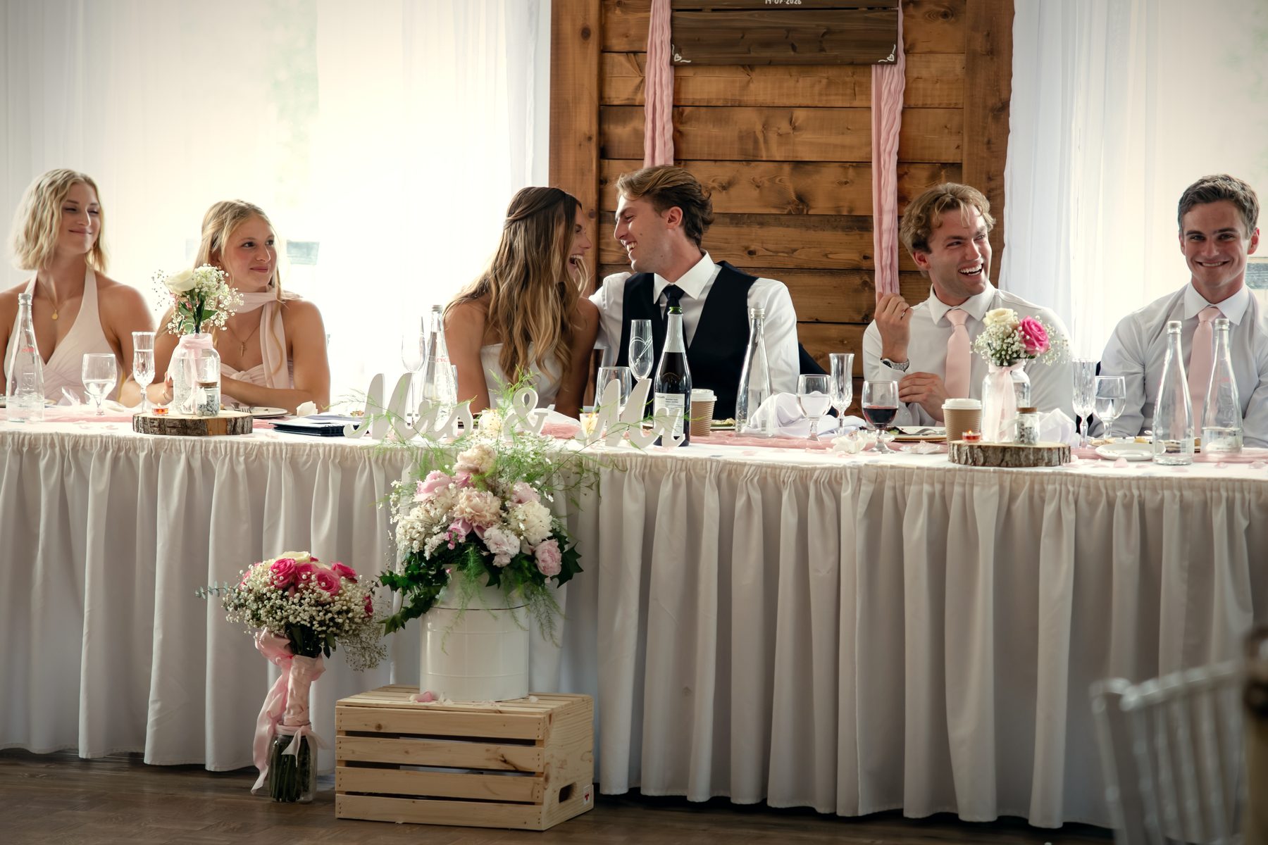 The head table against the wood feature wall, the couple laughing with their wedding party