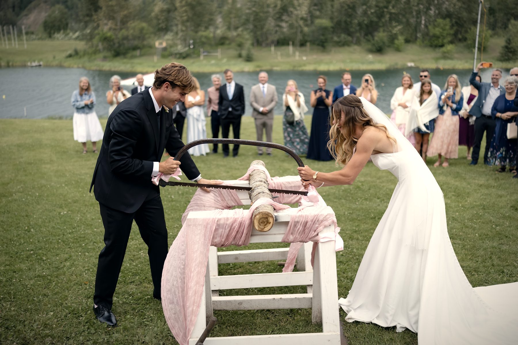 The couple sawing a log together after the ceremony, a tradition their guests watch from the lawn