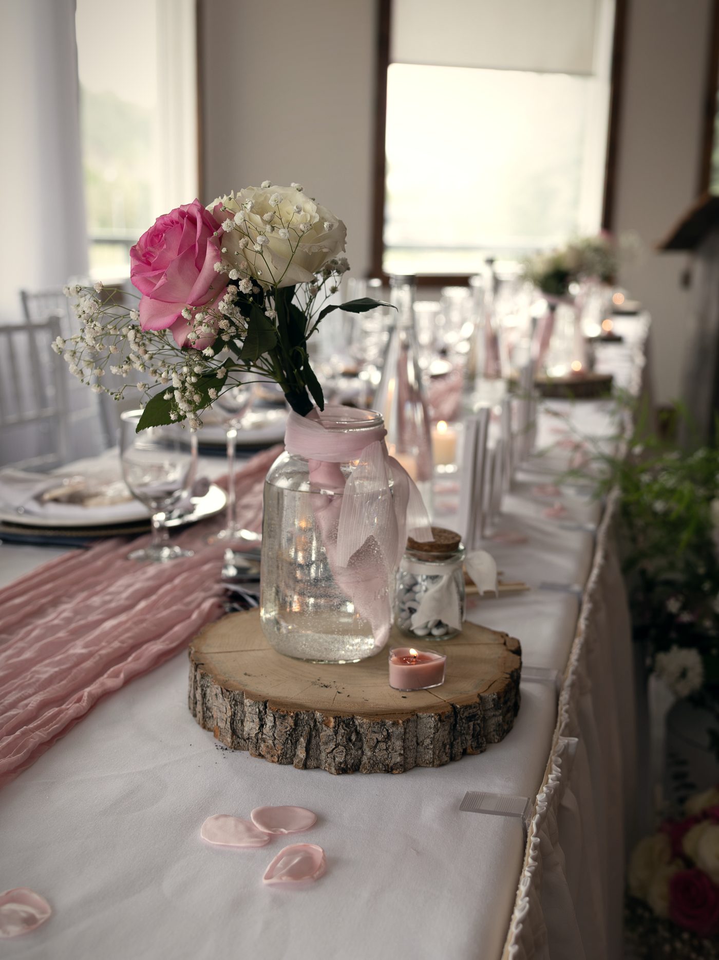 A single pink rose in a jar on the head table, window light behind it