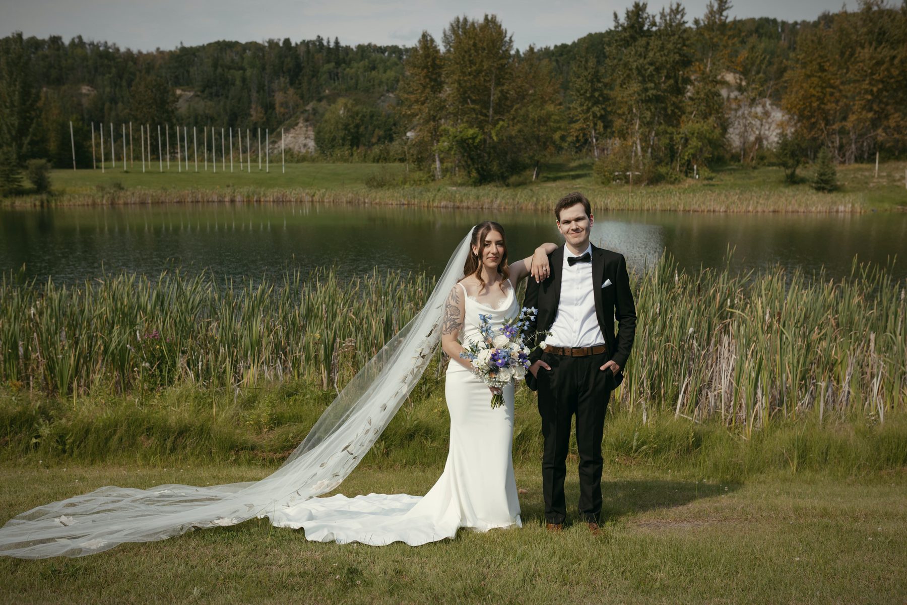 A couple on the shore, the bride's long veil trailing across the grass