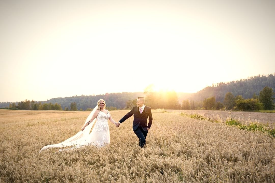 A bride and groom running hand in hand through a wheat field at sunset, her veil trailing behind