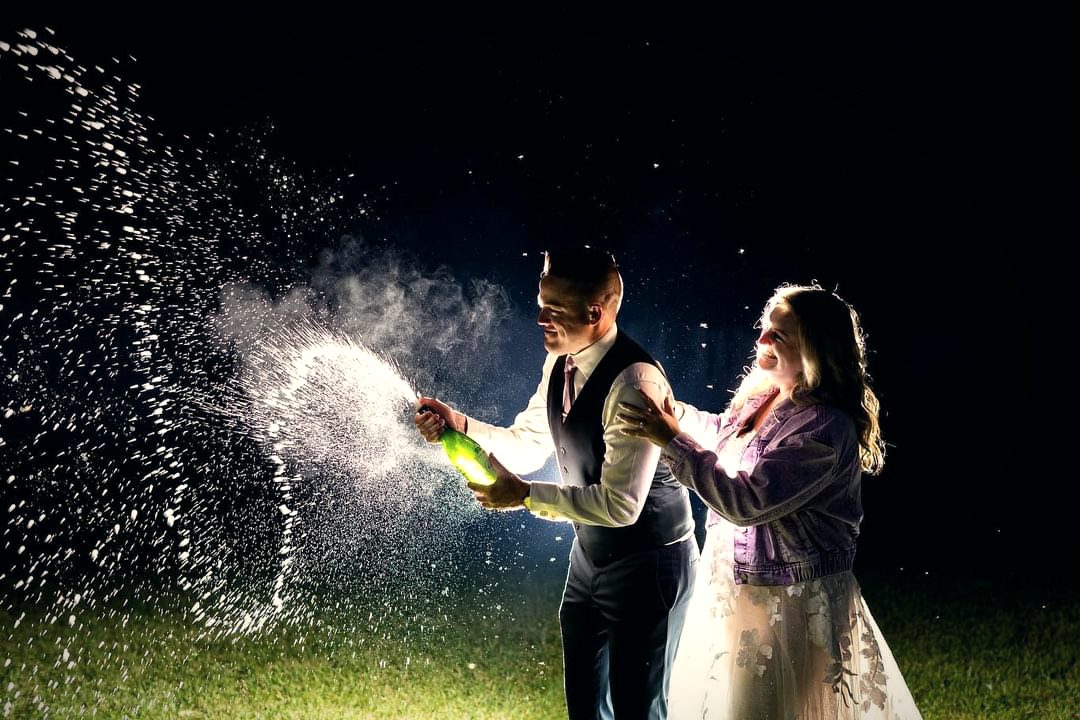A couple at night, a bottle of champagne sprayed into the dark air between them