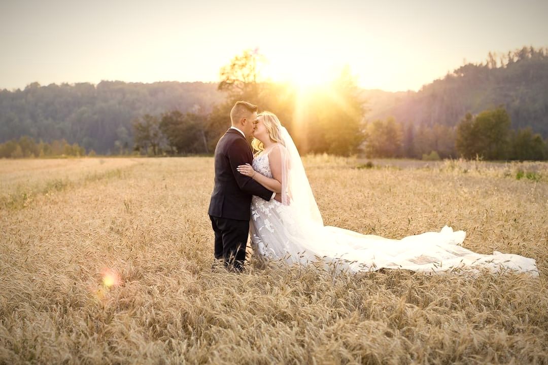 A couple embracing in a golden field at sunset, the sun flaring behind them and her veil spread on the grass