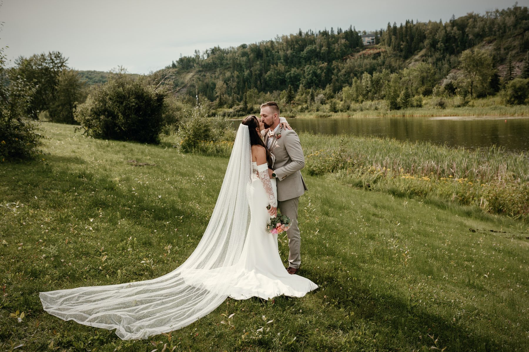 A kiss on the hillside above the lake, the bride's long veil trailing across the grass