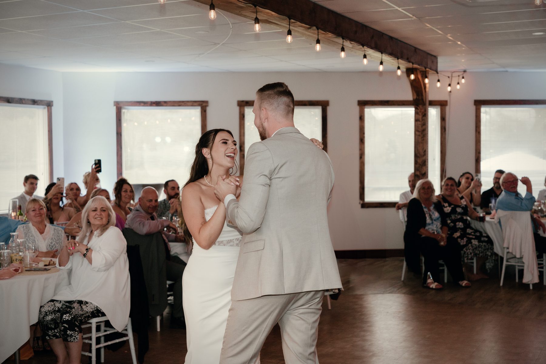 The first dance in the hall, guests watching from the round tables under the timber beams