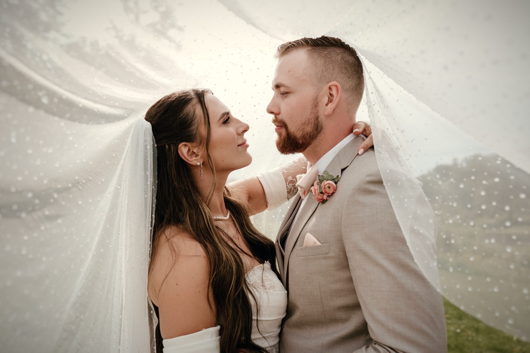 A couple a breath apart beneath the bride's veil, the sky pale behind the lace