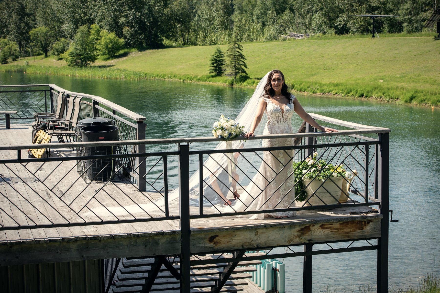 A bride leaning on the dock railing above the water, her bouquet beside her
