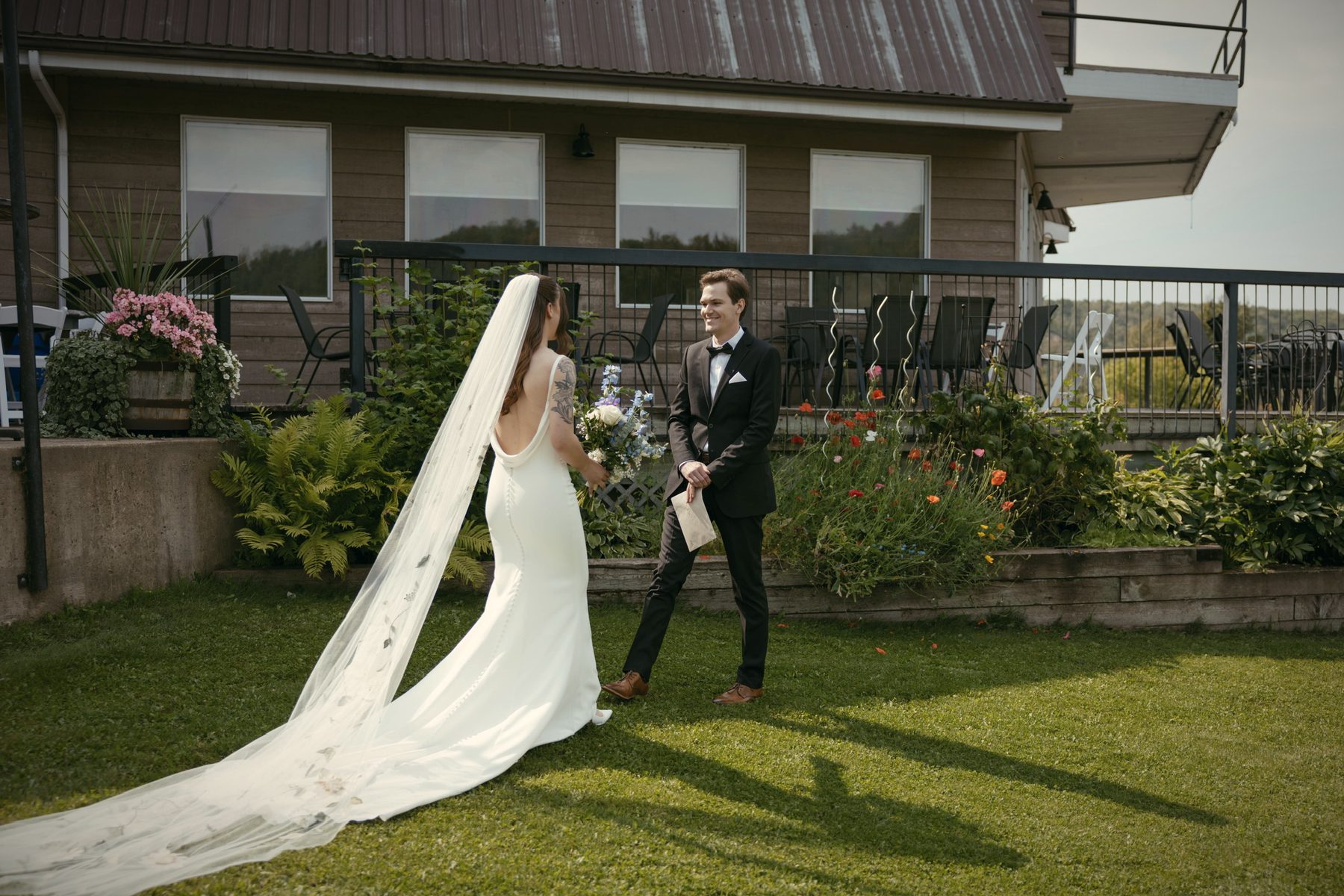 A groom and bride walking toward the lodge on the lawn, her long veil trailing behind