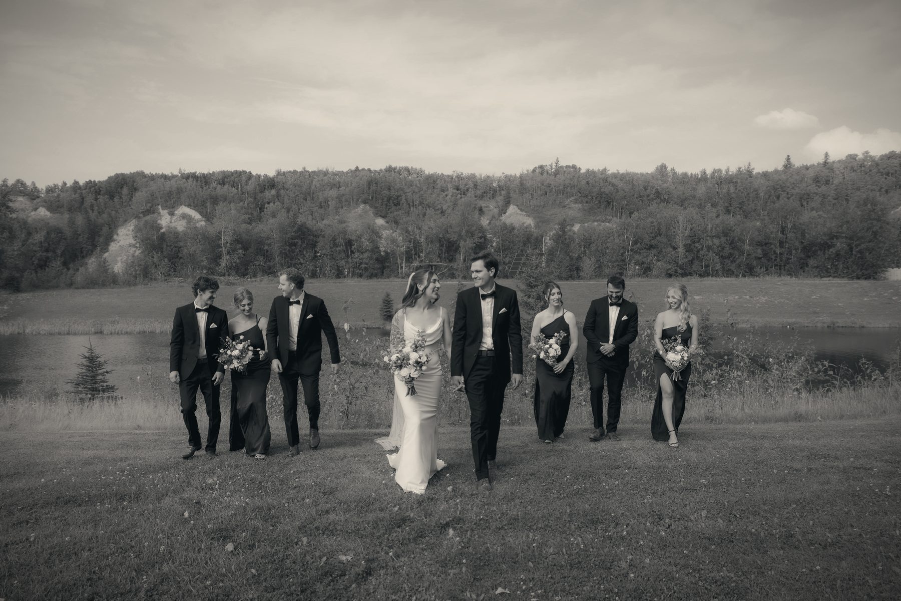 A black and white frame of the wedding party walking together across the field