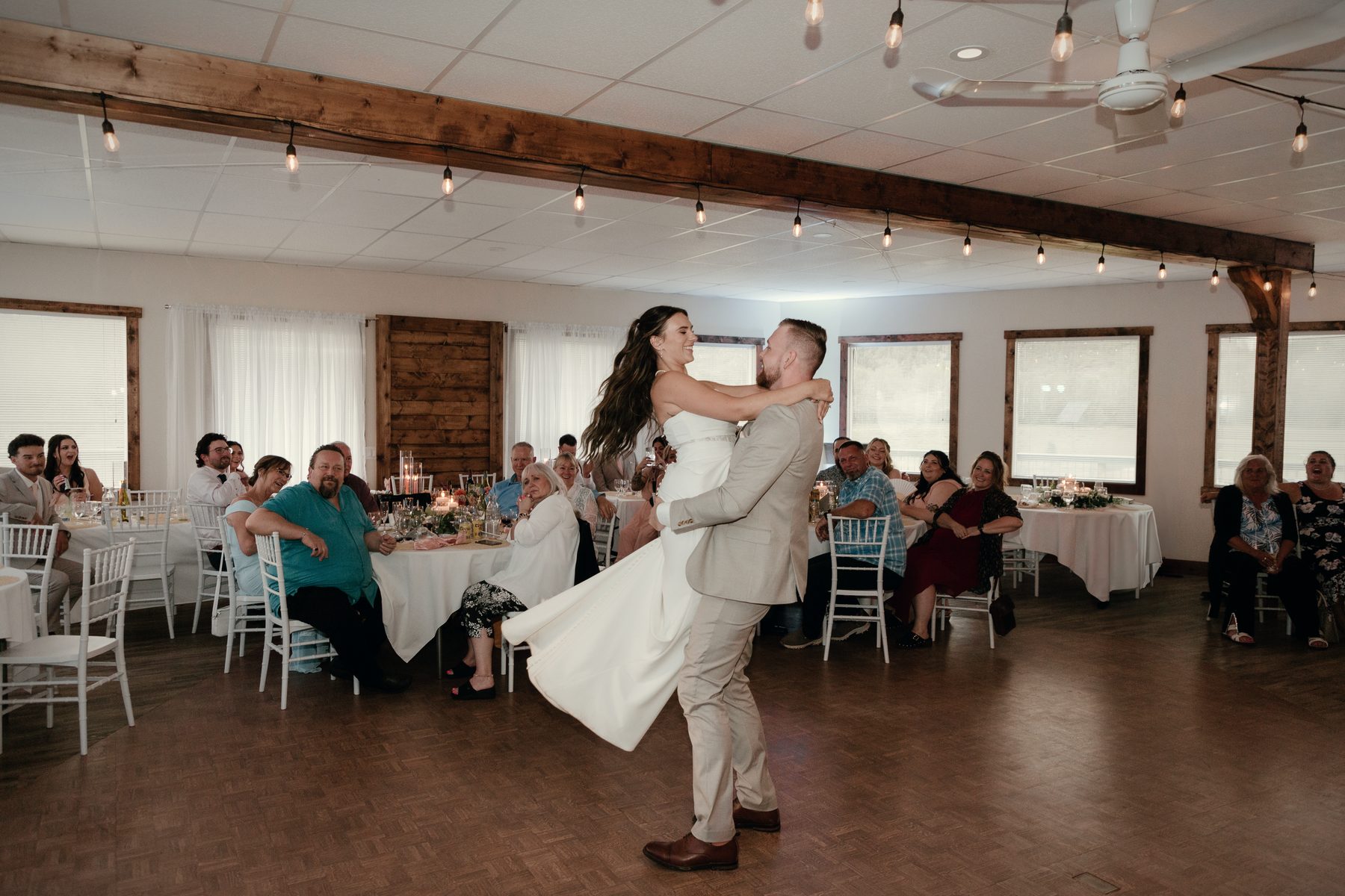 A first dance in the hall, the couple turning under the timber beam while guests watch from their tables
