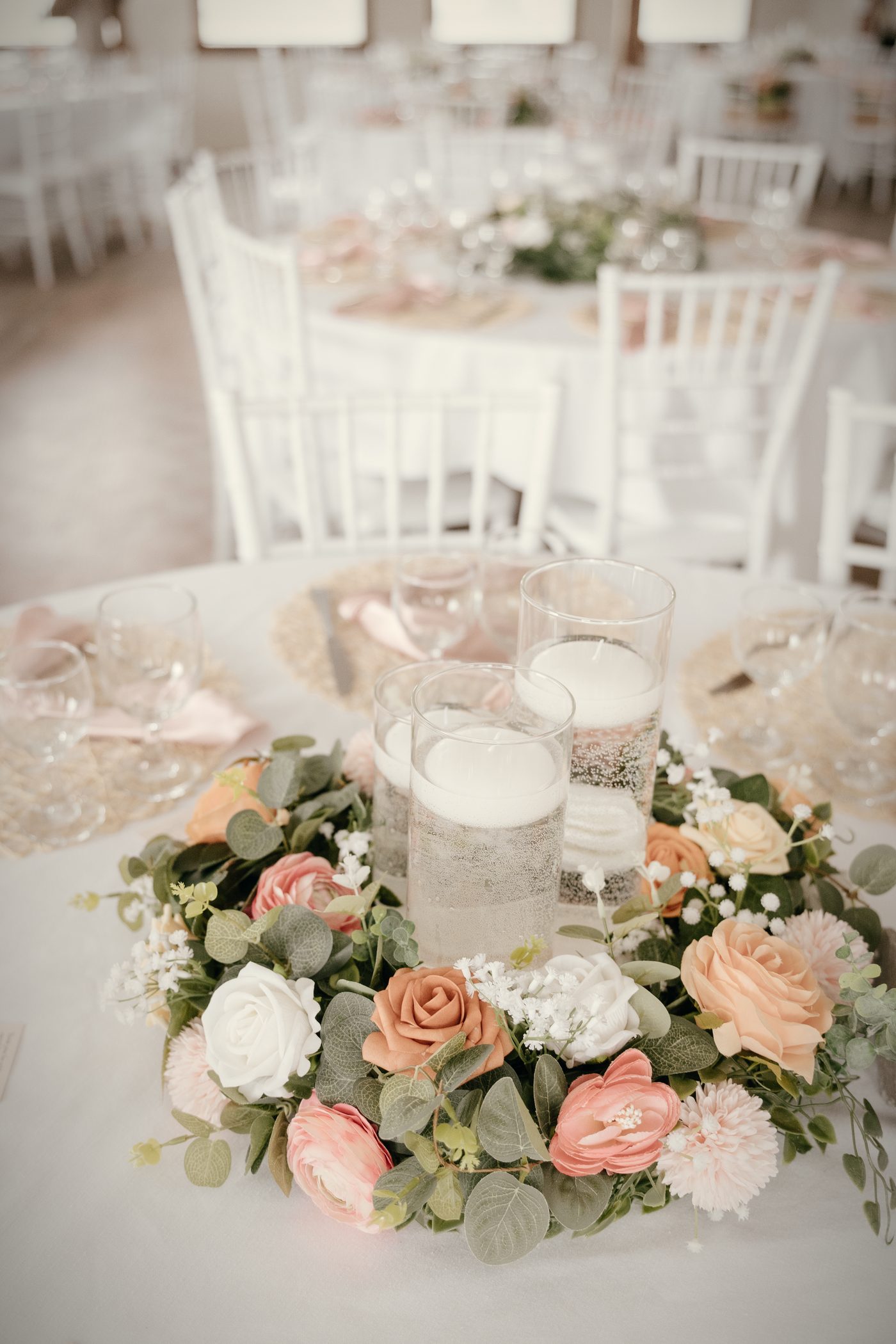 A low wreath of peach and blush roses around three candles on a white-clothed round table