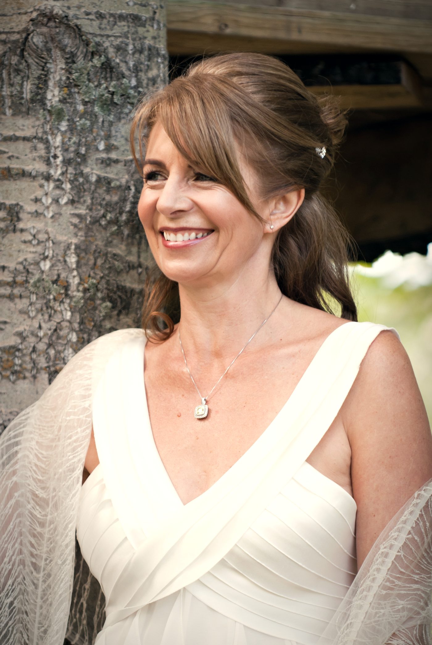 A bride laughing outdoors, her hair pinned up, a pendant at her collarbone