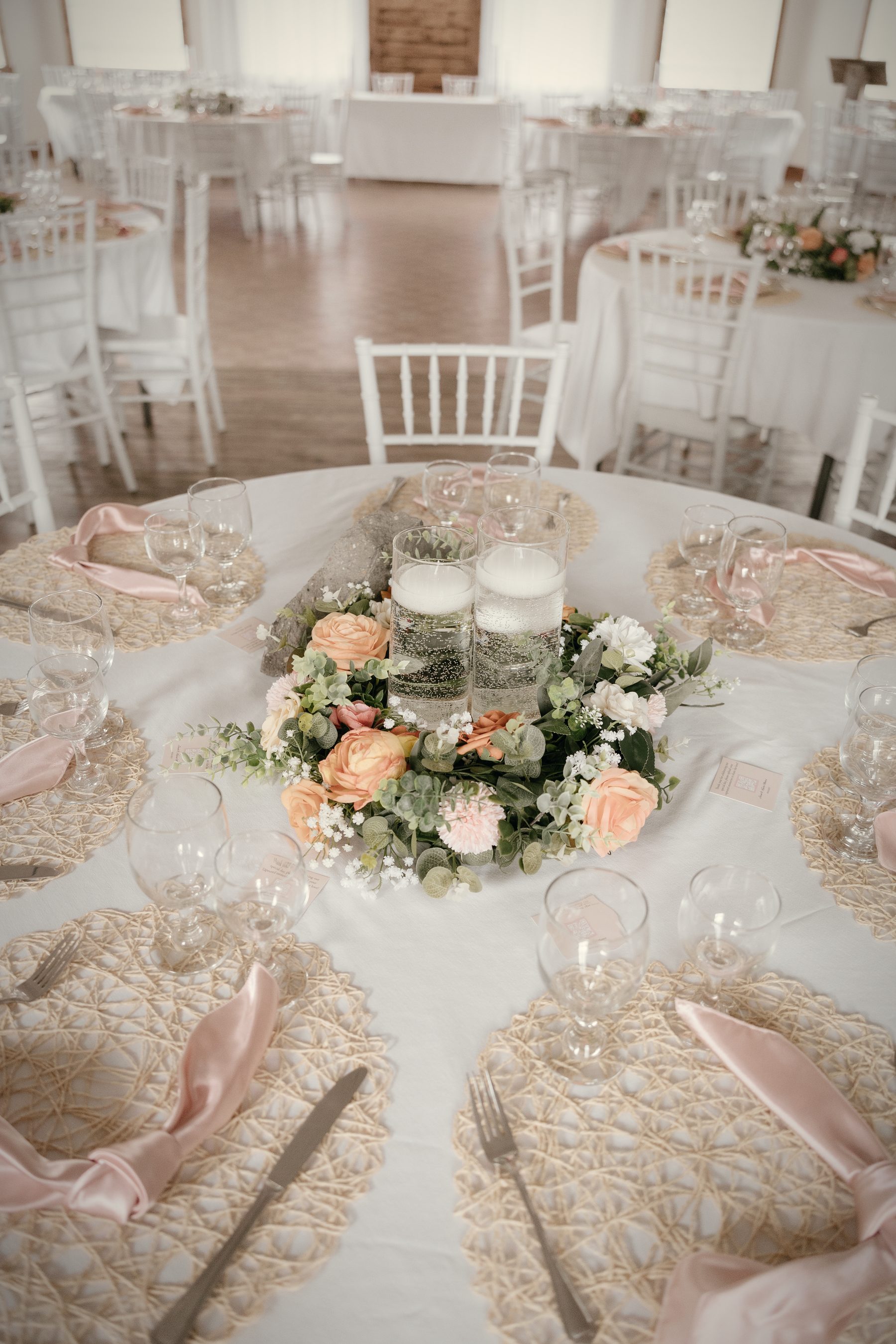 A round table set for dinner, a ring of peach and white florals at its centre and more tables beyond