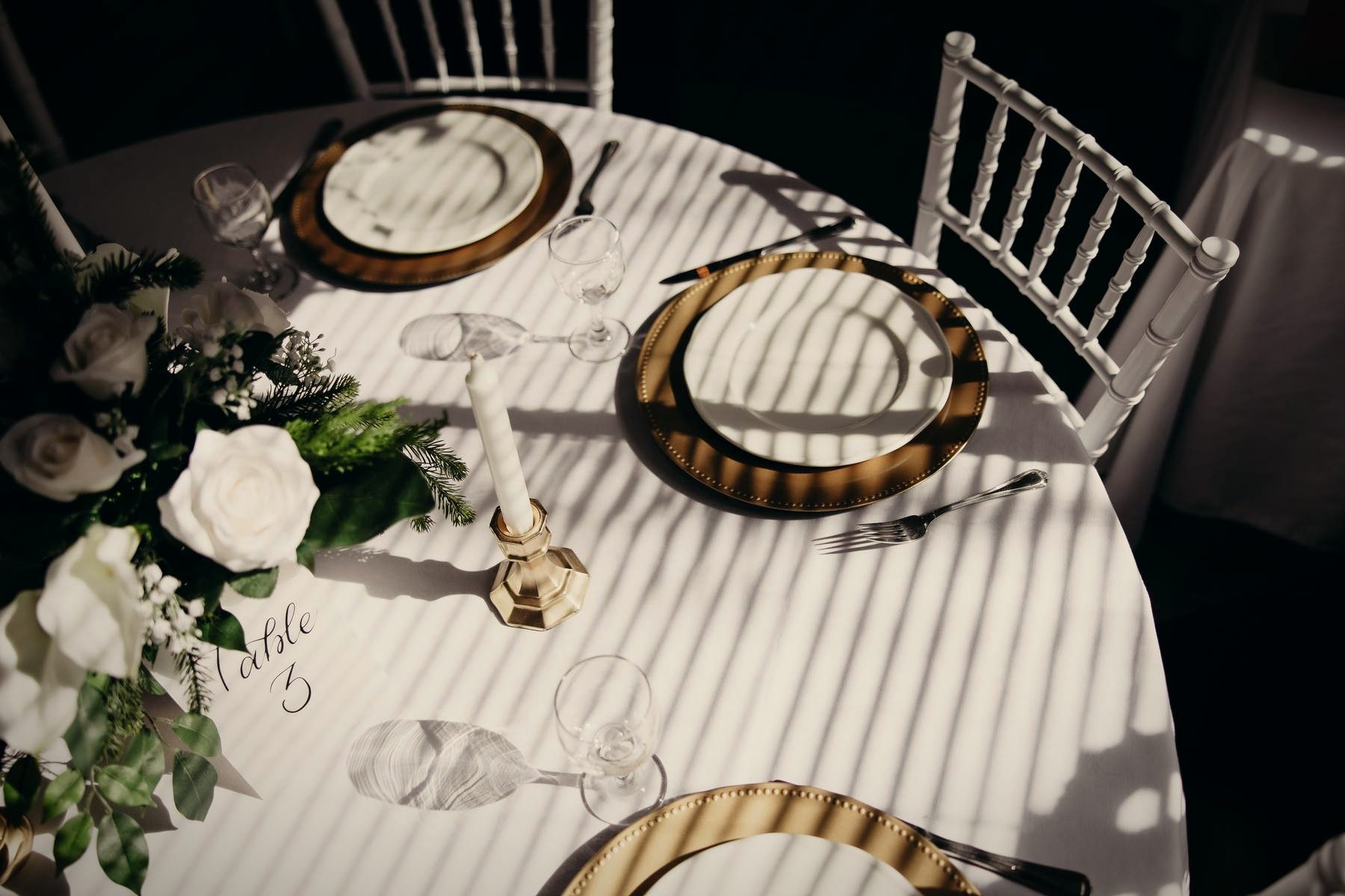 A table seen from above: gold chargers, white roses, candles and soft linen