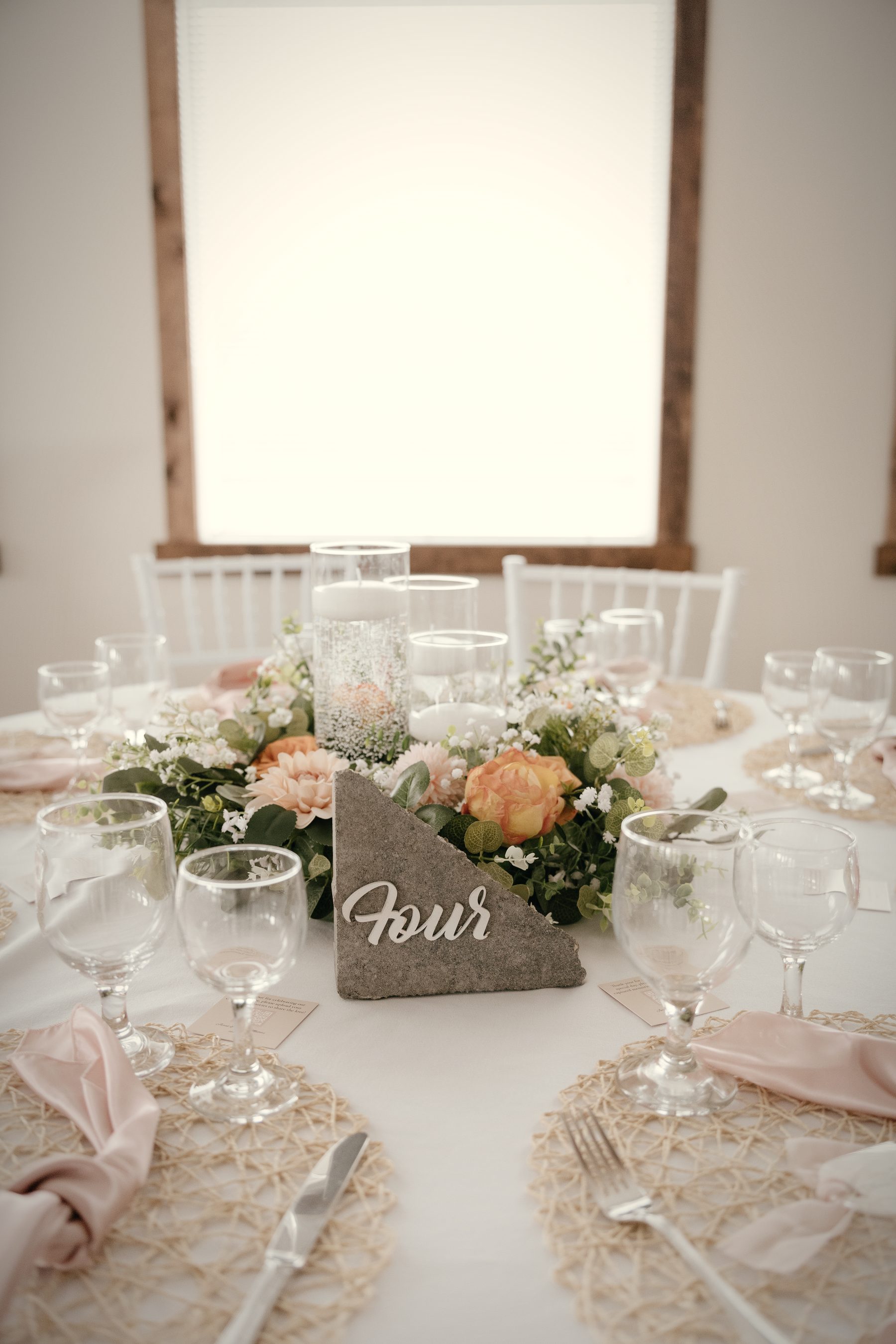 A centrepiece with a stone table number, white chairs and a bright window behind it
