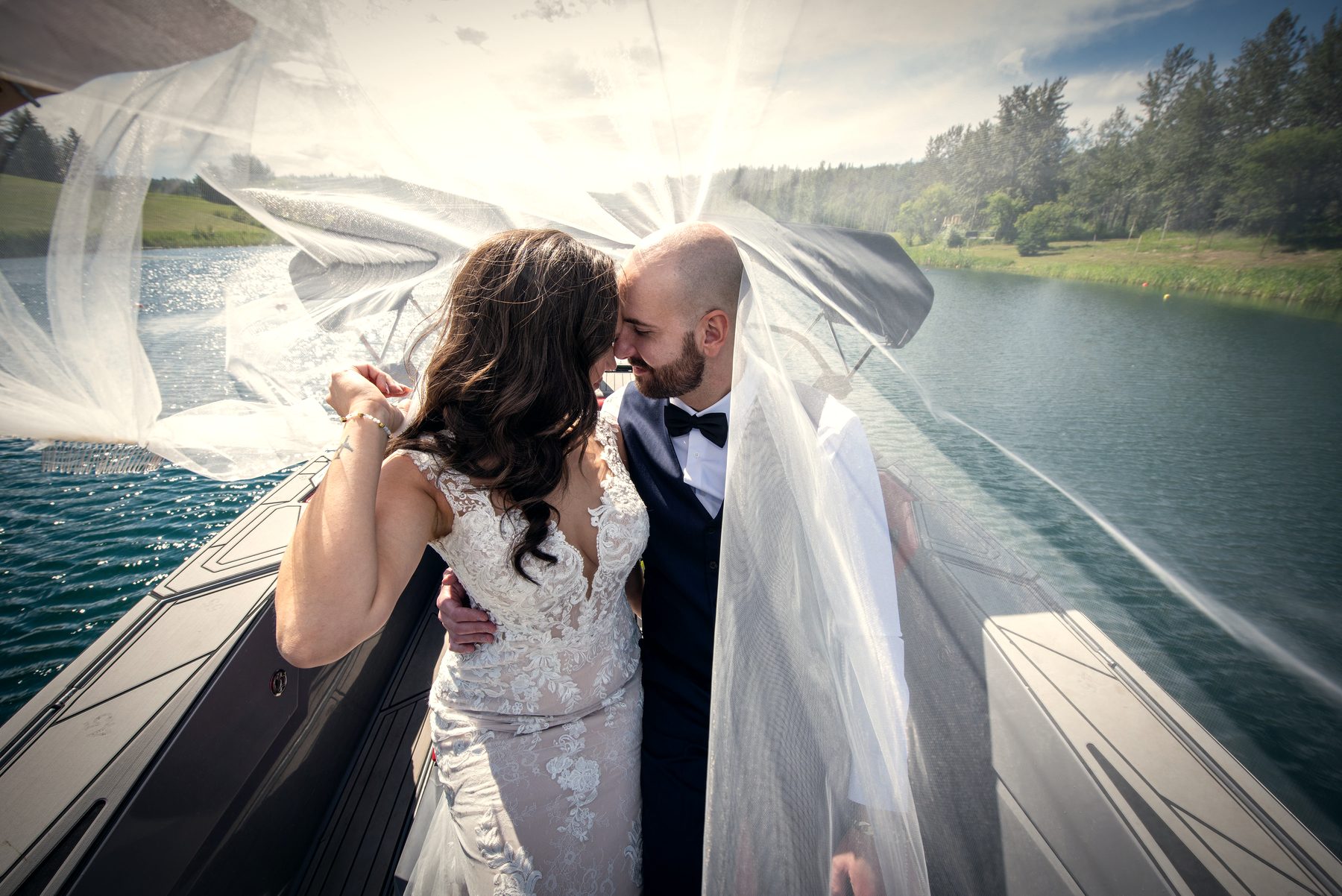 A bride and groom laughing together under her veil in the boat, the lake behind