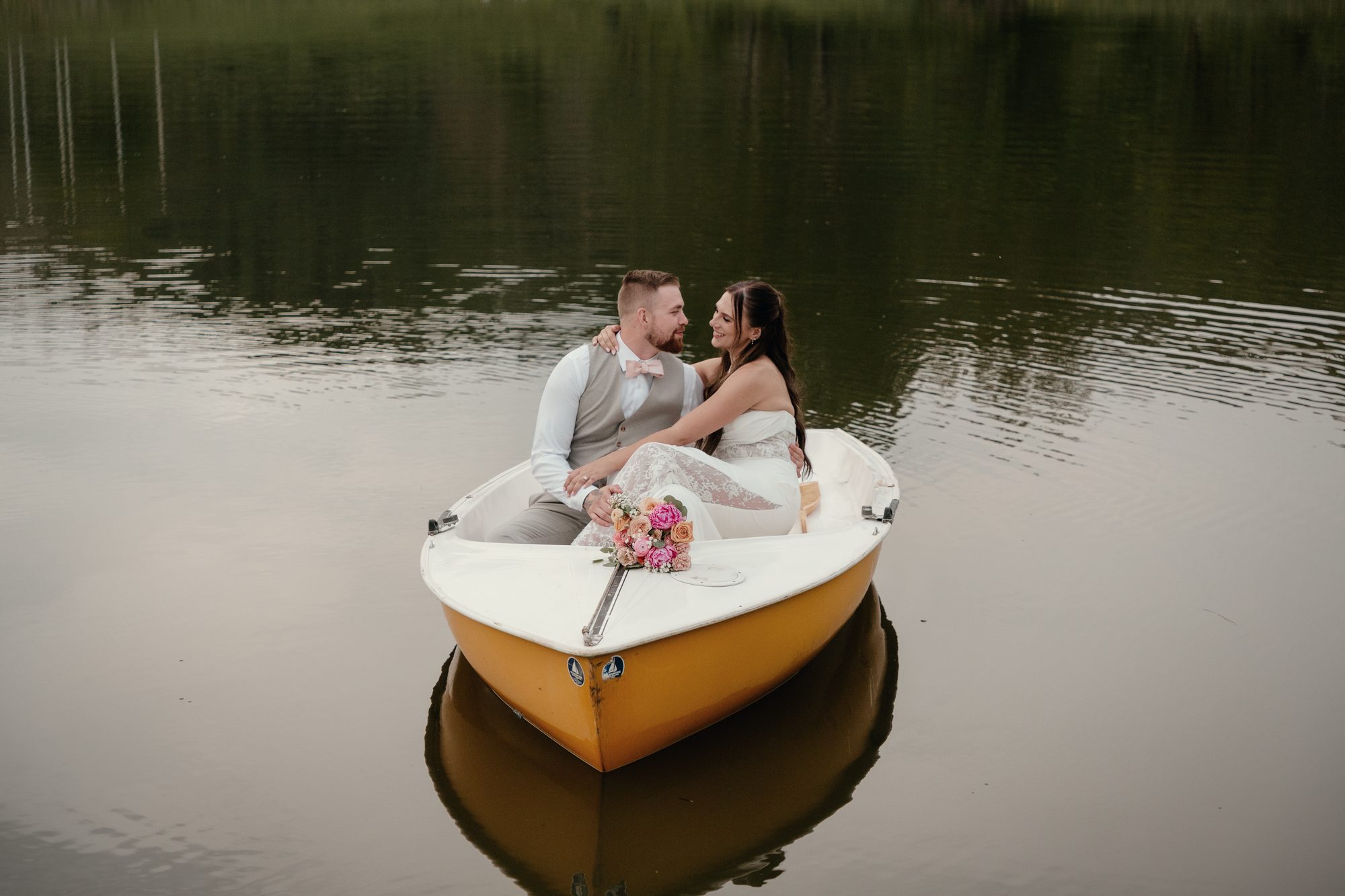 A couple in a yellow rowboat on dark water, the bride's bouquet on the bow