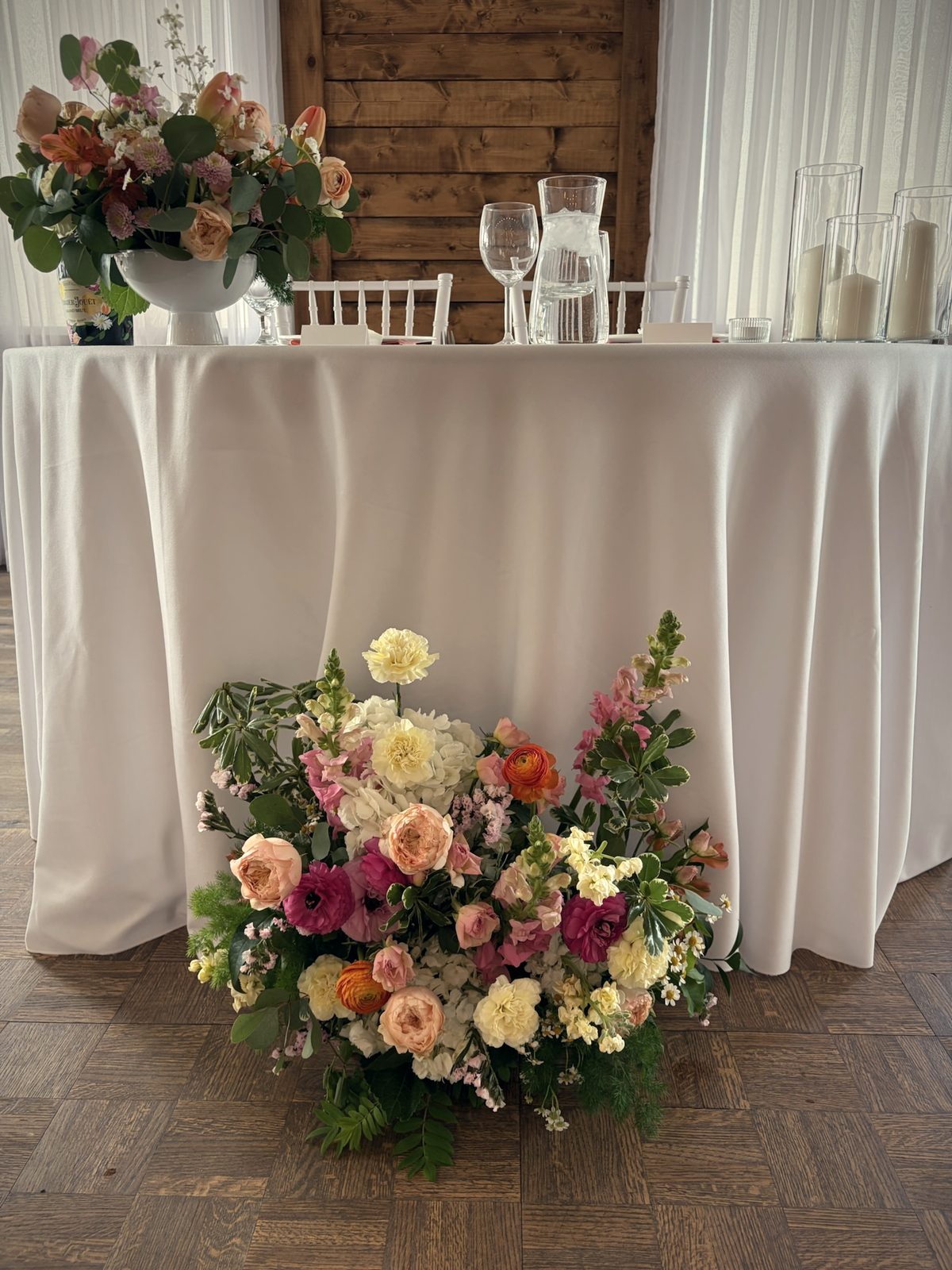 A large arrangement of peach, pink and cream roses on the floor beside a round table