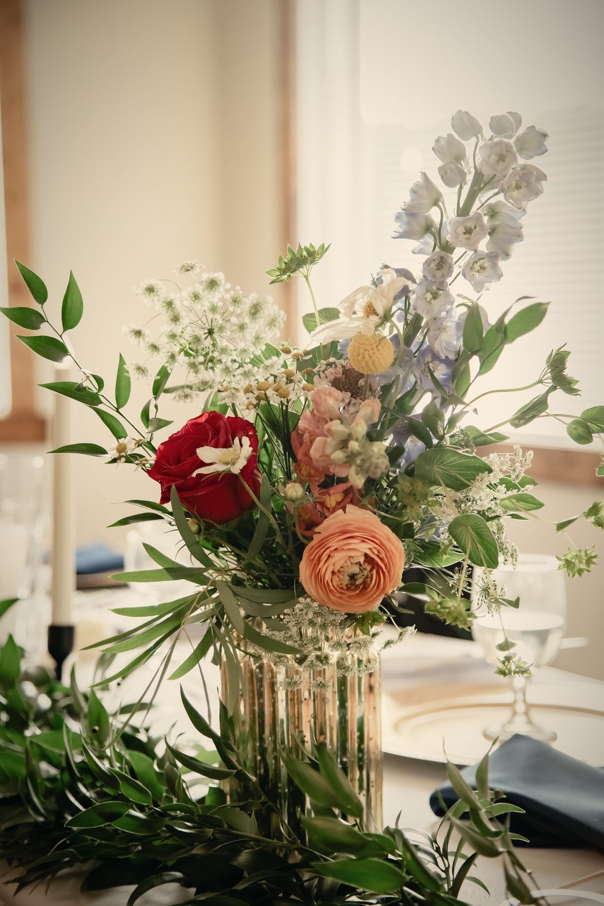 Red and orange ranunculus and wildflowers in a tall gold vase