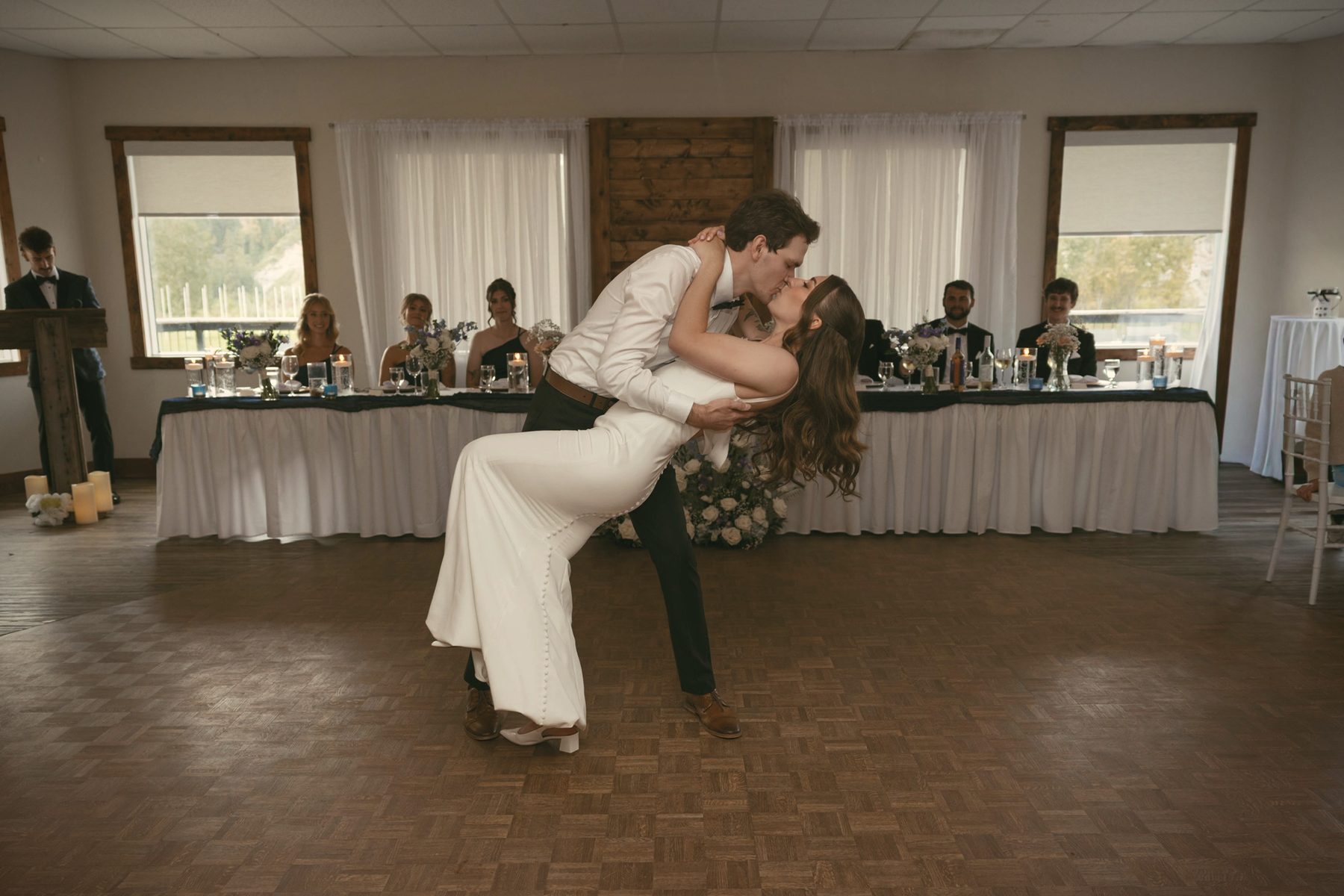 A groom dipping his bride on the hall floor, the head table and guests behind them