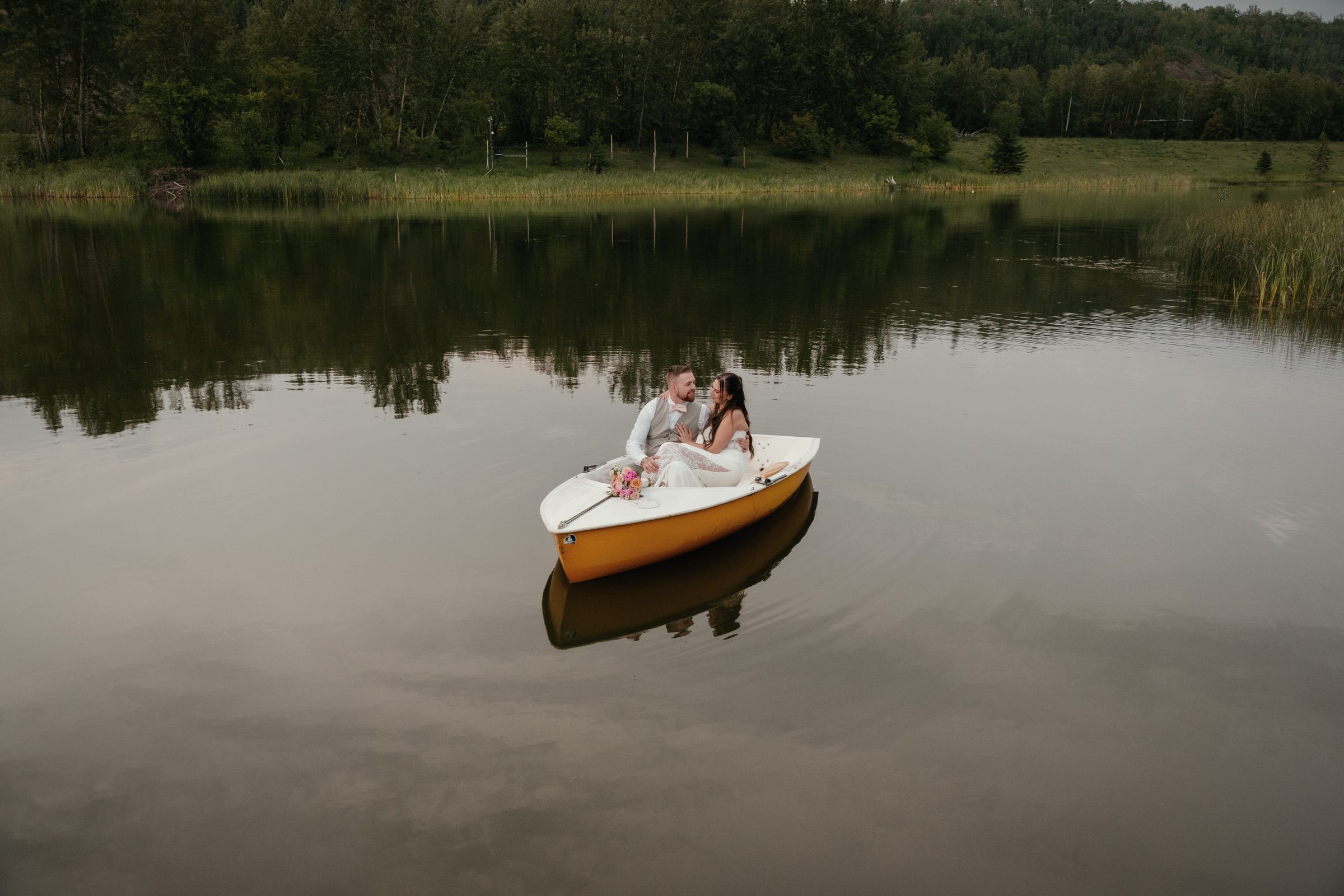 A couple sitting close in a small yellow rowboat, alone on the dark, still water of the lake