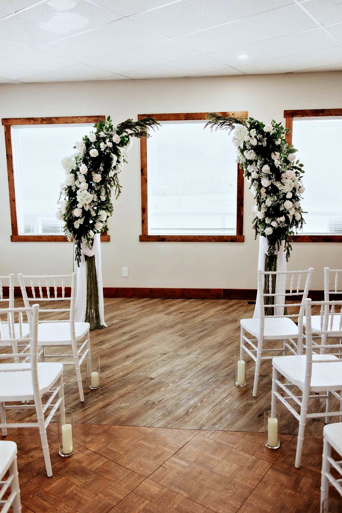An indoor ceremony set in the hall, a floral arch and white chairs by the windows