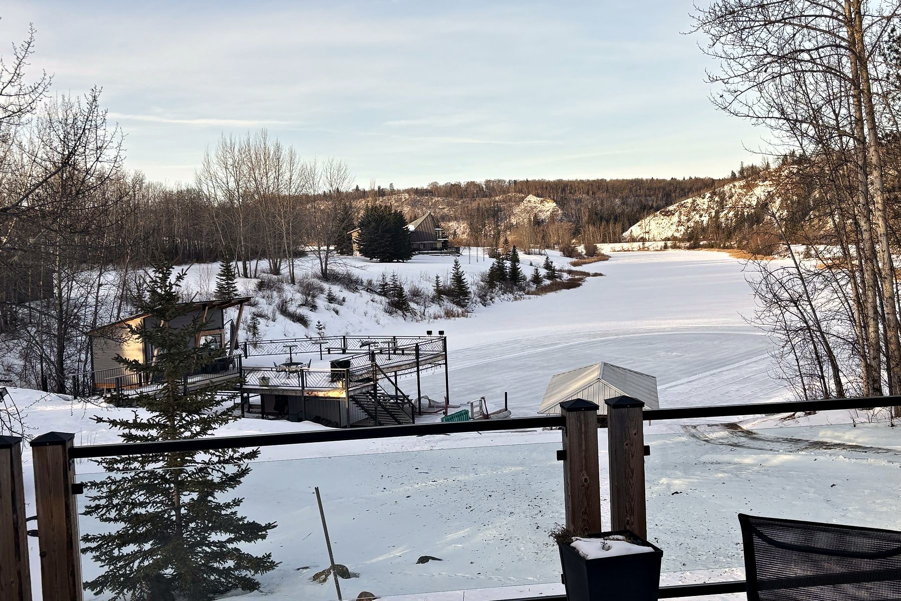The deck in winter, railing and chairs under snow, the frozen lake below