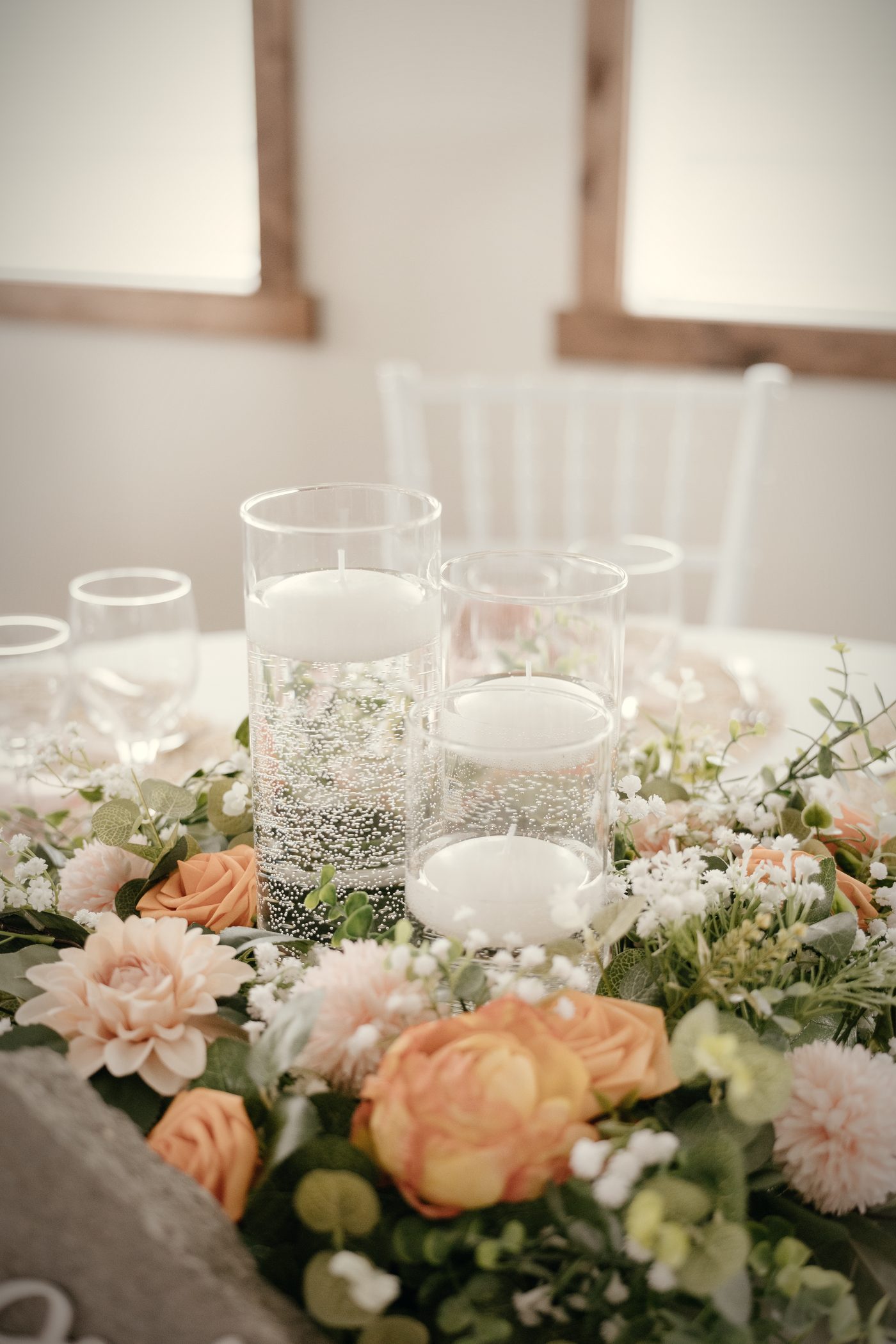 Floating candles in glass cylinders among peach garden roses and baby's breath
