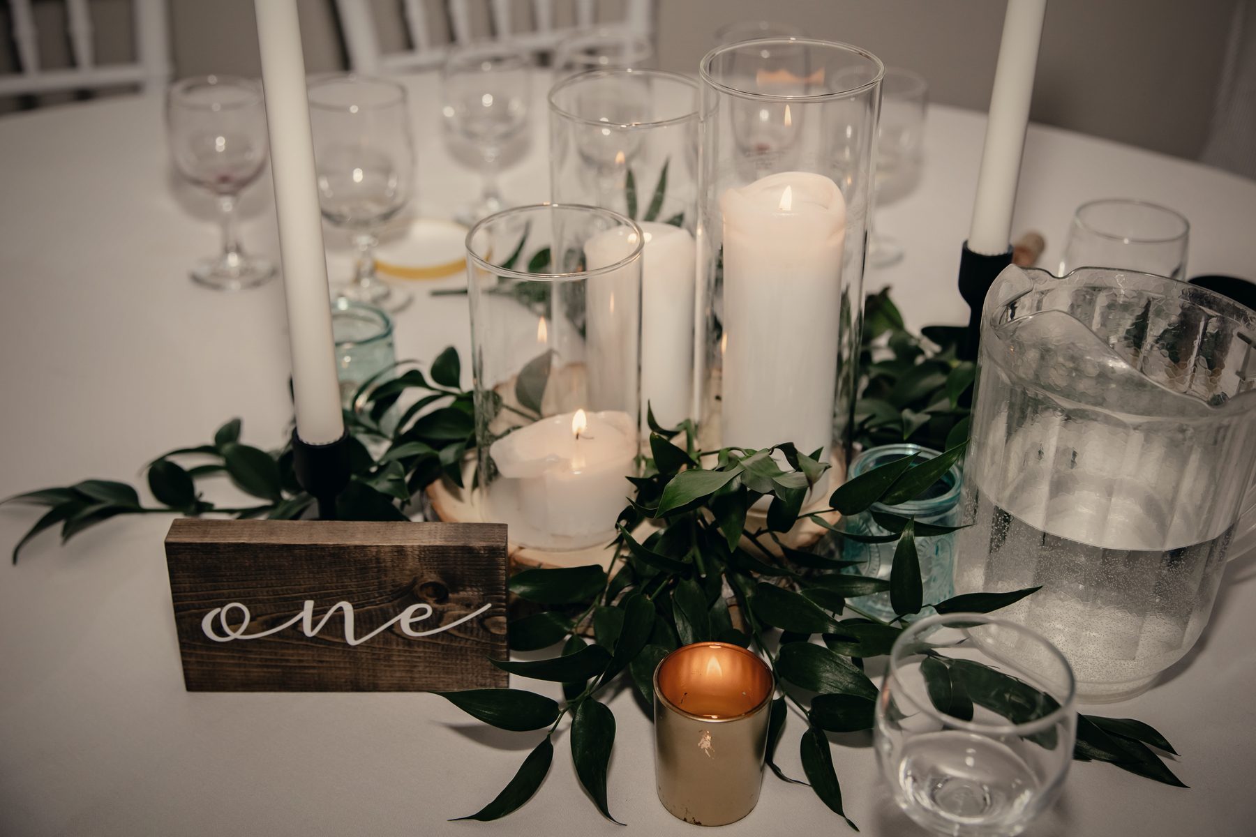 A wooden table number among pillar candles, greenery and glass
