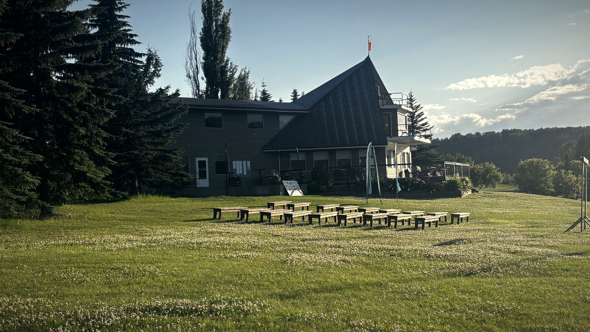 The hall from the lawn in evening light, the ceremony benches set in rows on the grass below it