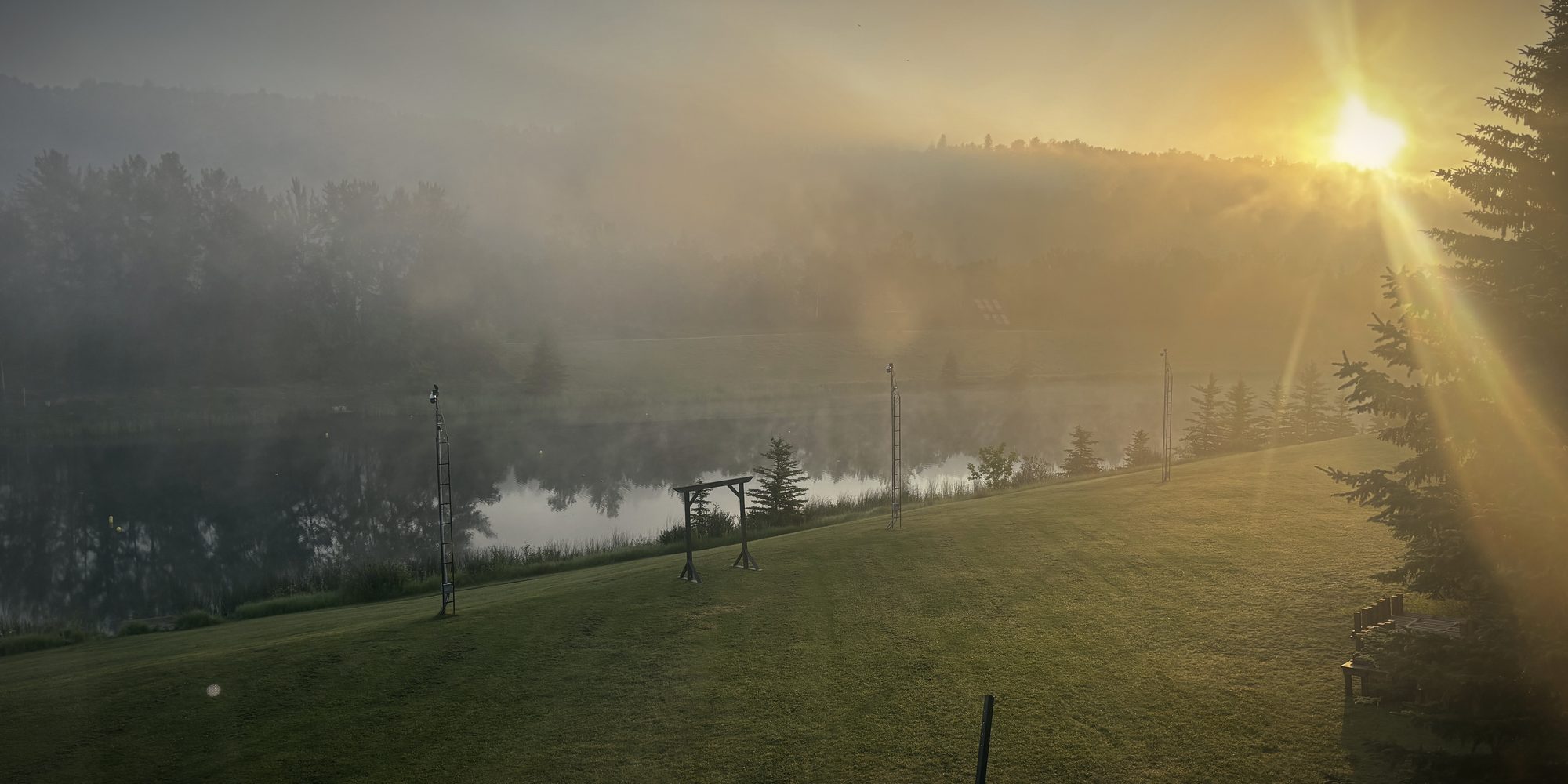 The sun breaking through mist over the lake at dawn, the arbour and the lawn below