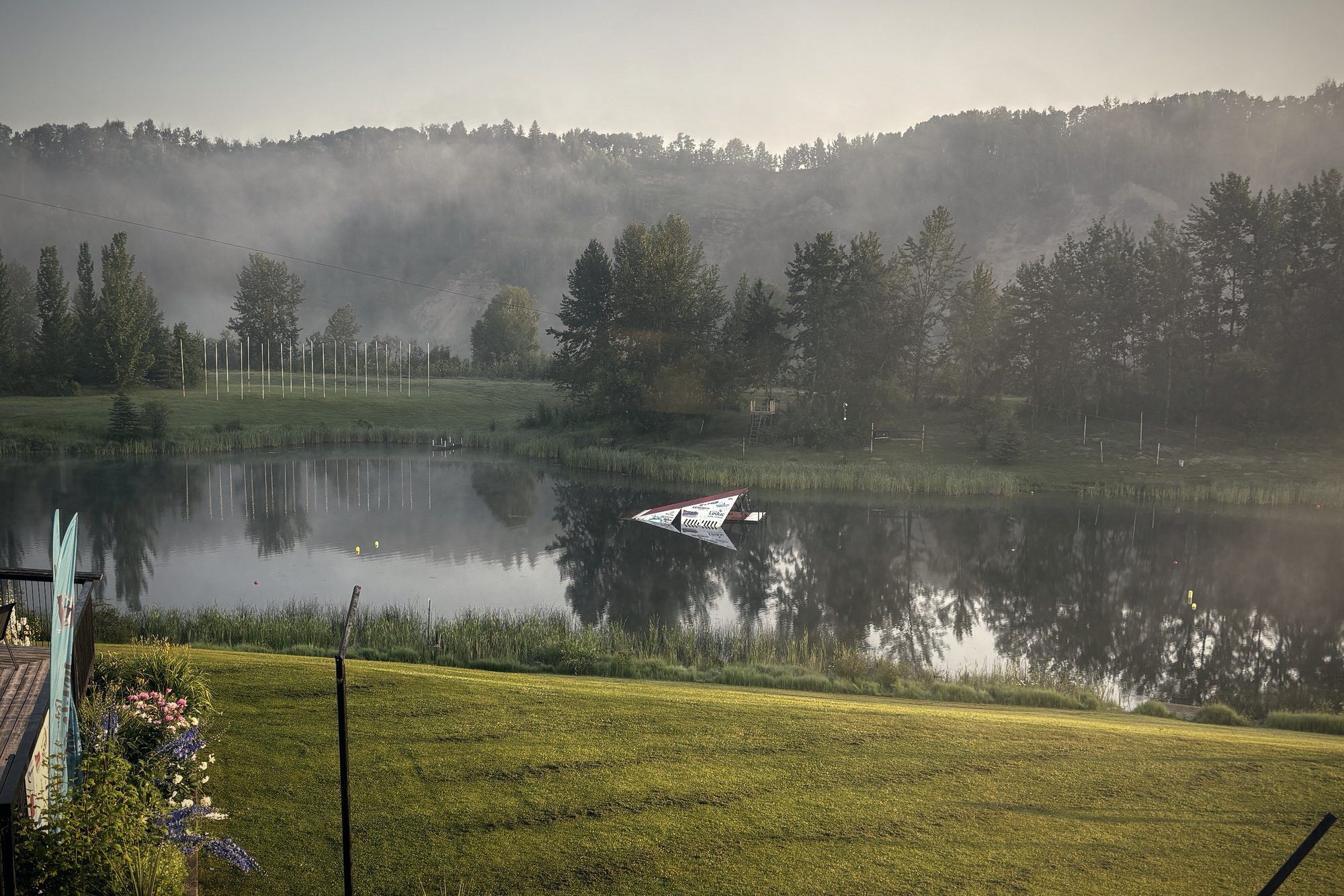 Mist on the lake at first light, seen from the deck, a ski boat idling on the still water
