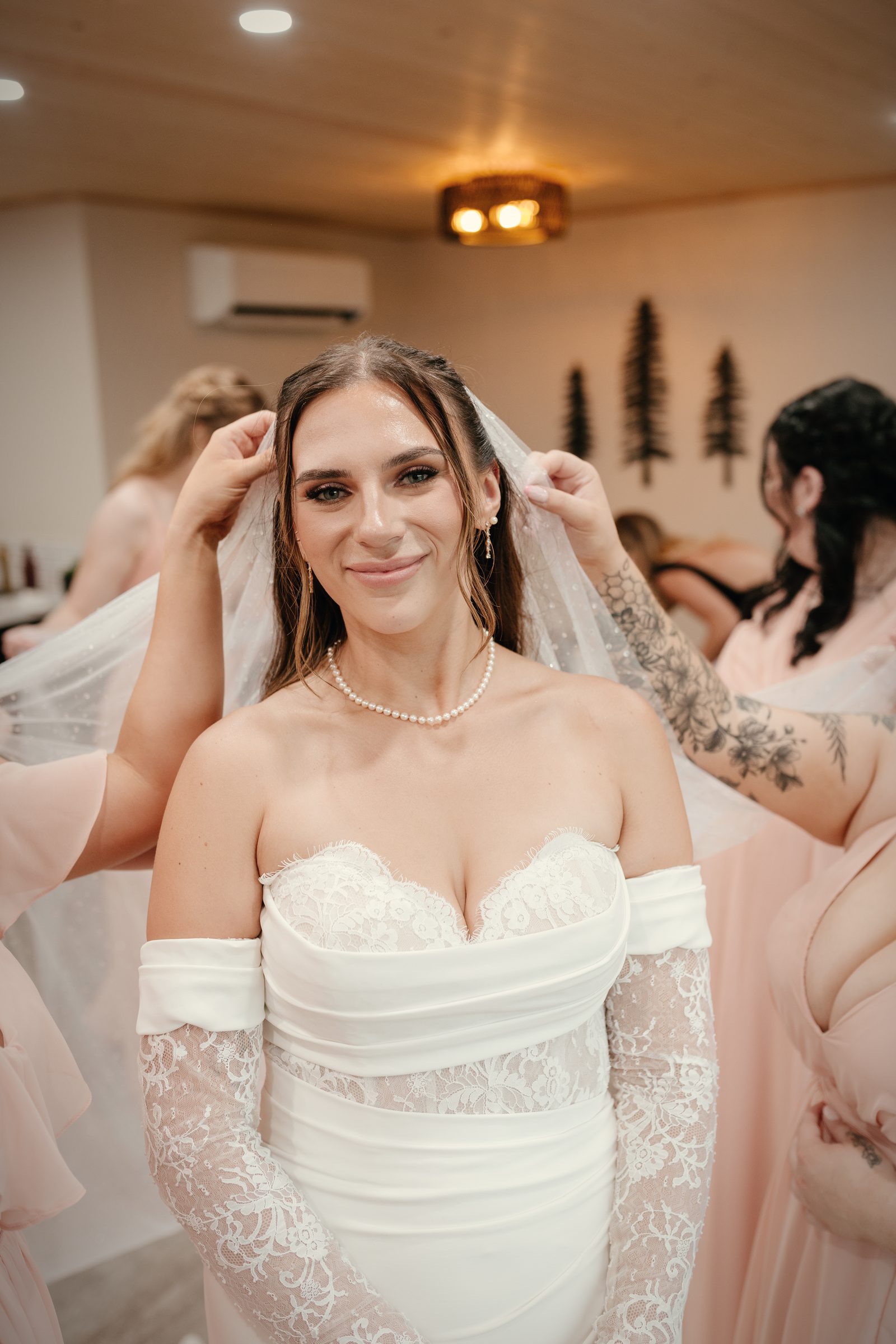 The bride smiling in the bridal suite as her bridesmaids set her veil, the wood-lined ceiling above them