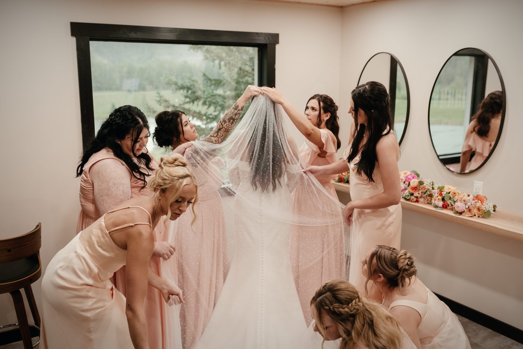 Getting ready in the bridal suite: bridesmaids lifting the veil beside the window and the round mirrors