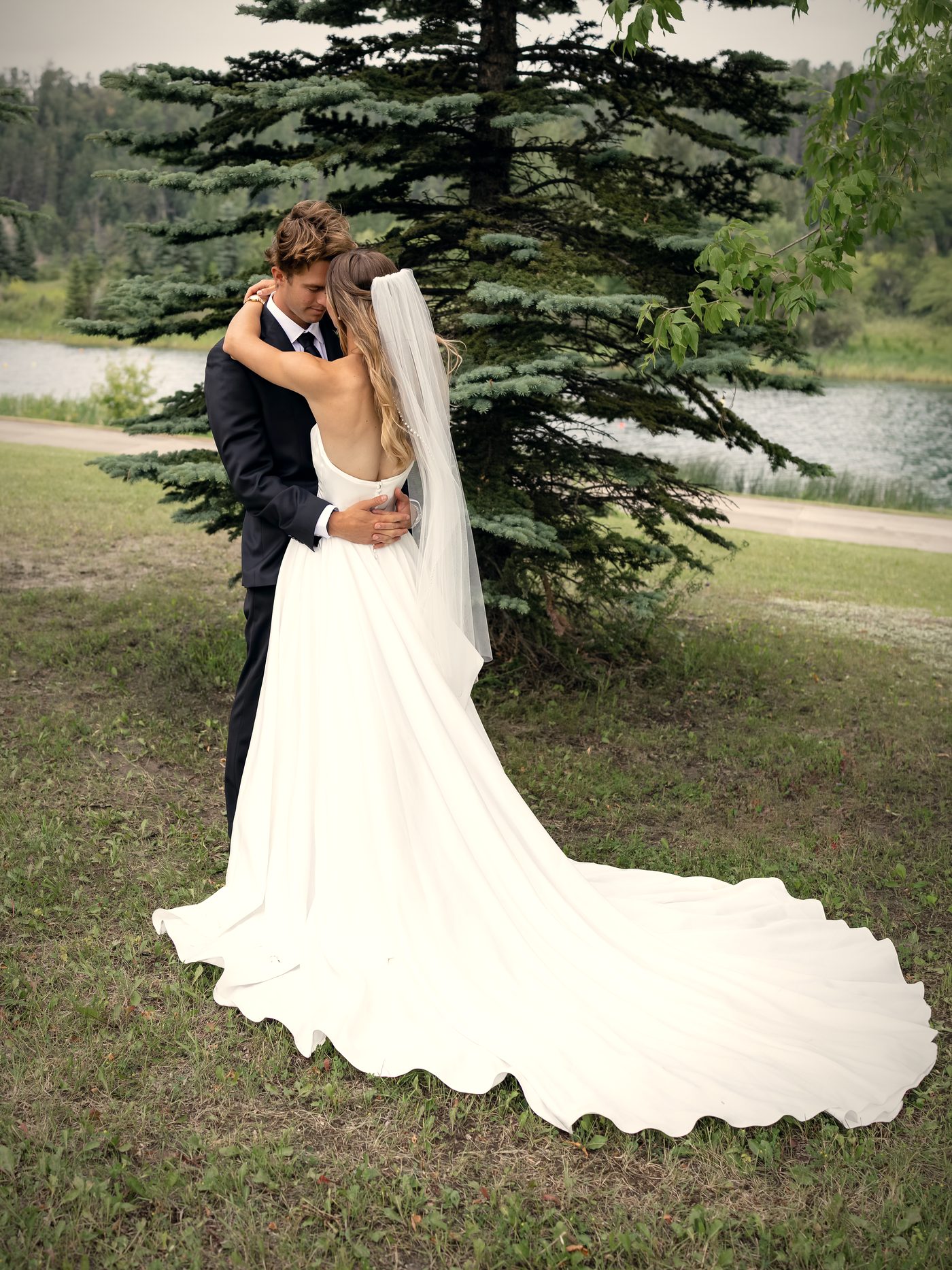 The couple beneath the big spruce after the ceremony, her train spread across the grass