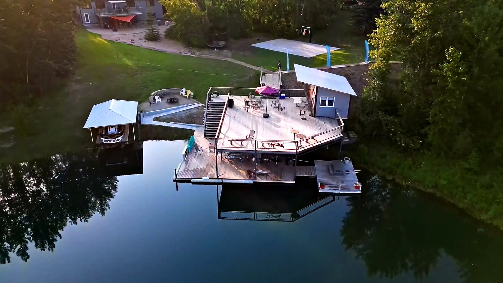 The deck and the dock from above at golden hour, the water flat and the hall behind
