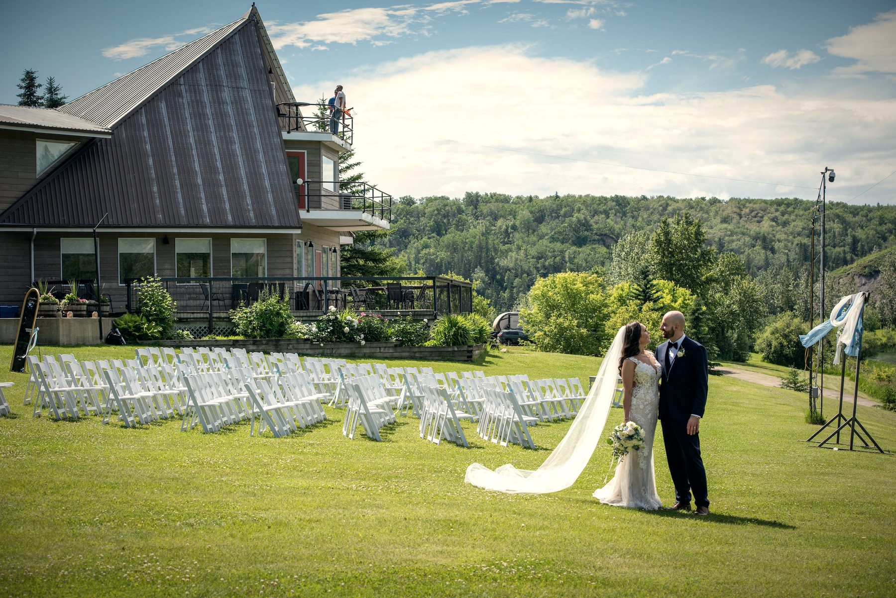 A couple kissing on the lawn in front of the lodge, rows of white chairs set behind them